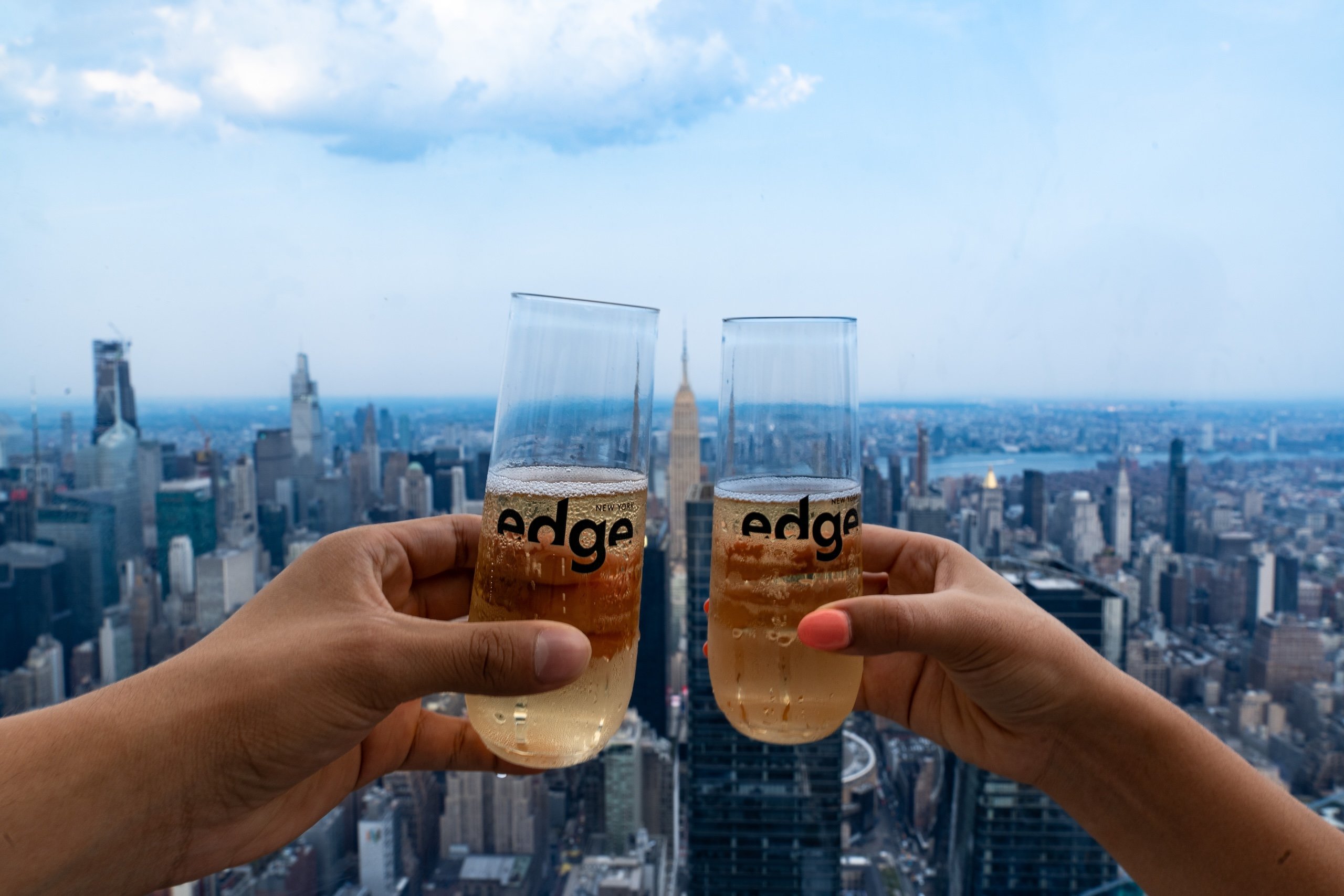Two people clink glasses with champagne overlooking New York city on a sunny day
