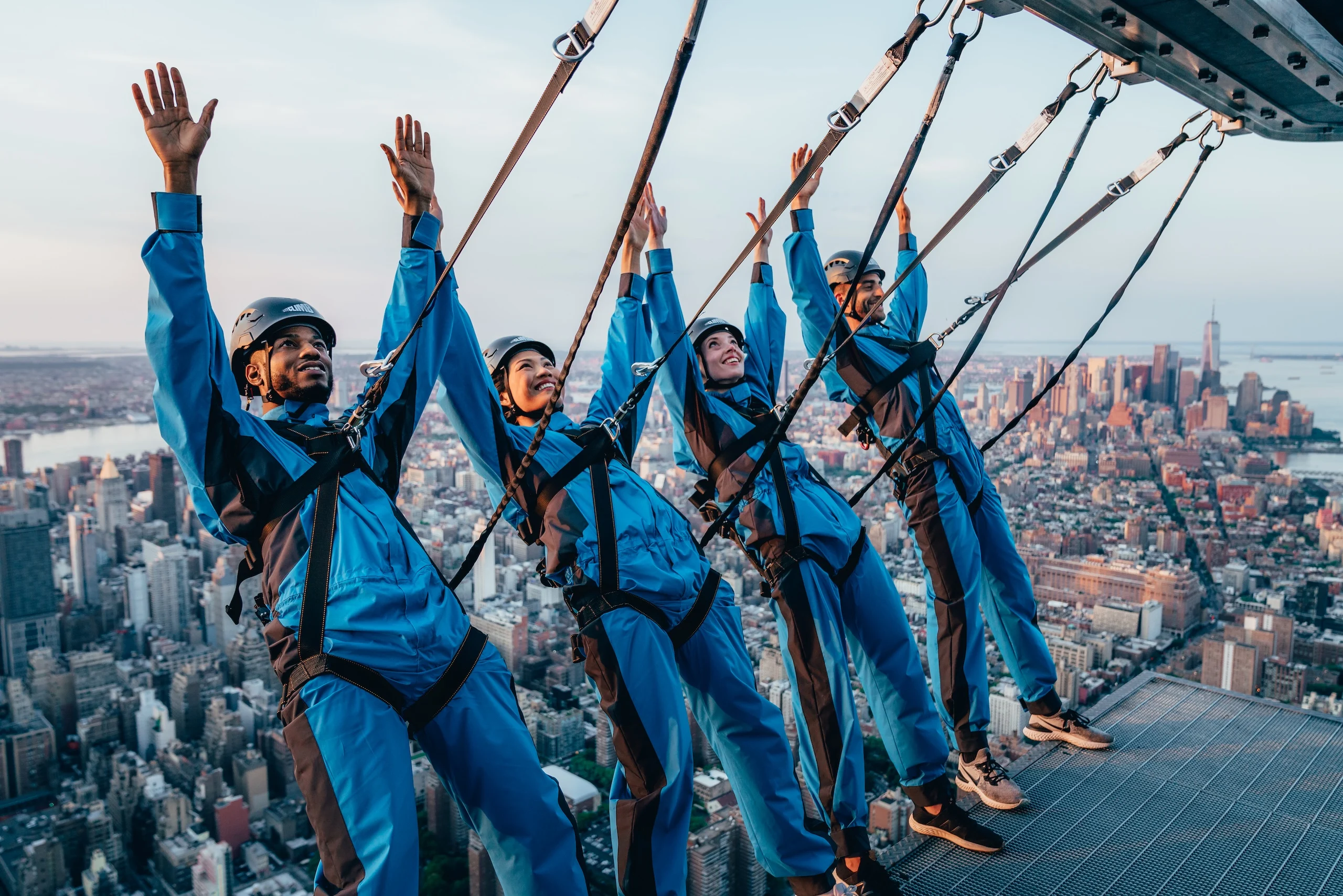 Four people raise their hands in the air in excitement as they lean back during City Climb at The Edge