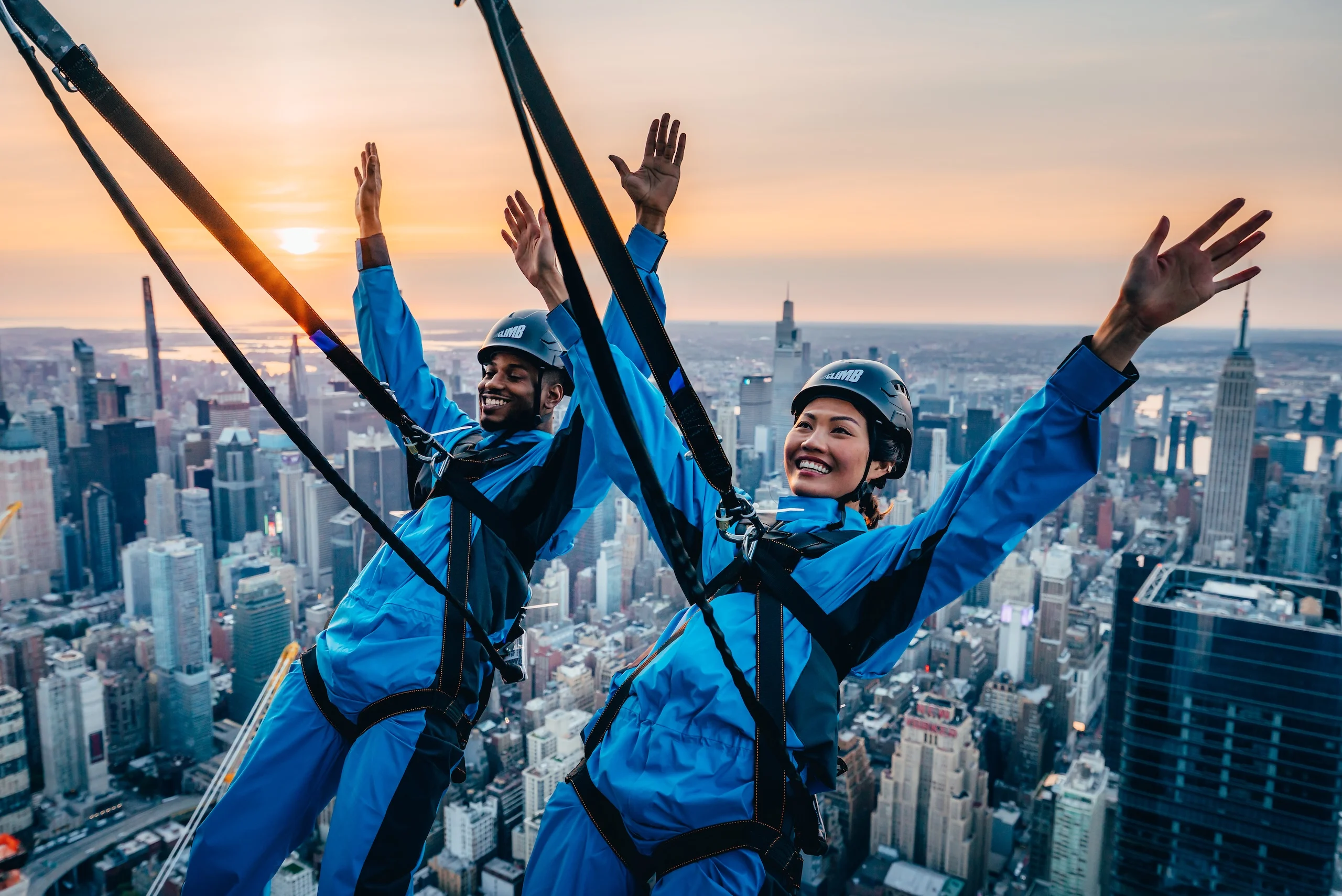 Two people raise their hands in the air in excitement as they lean back during City Climb at The Edge