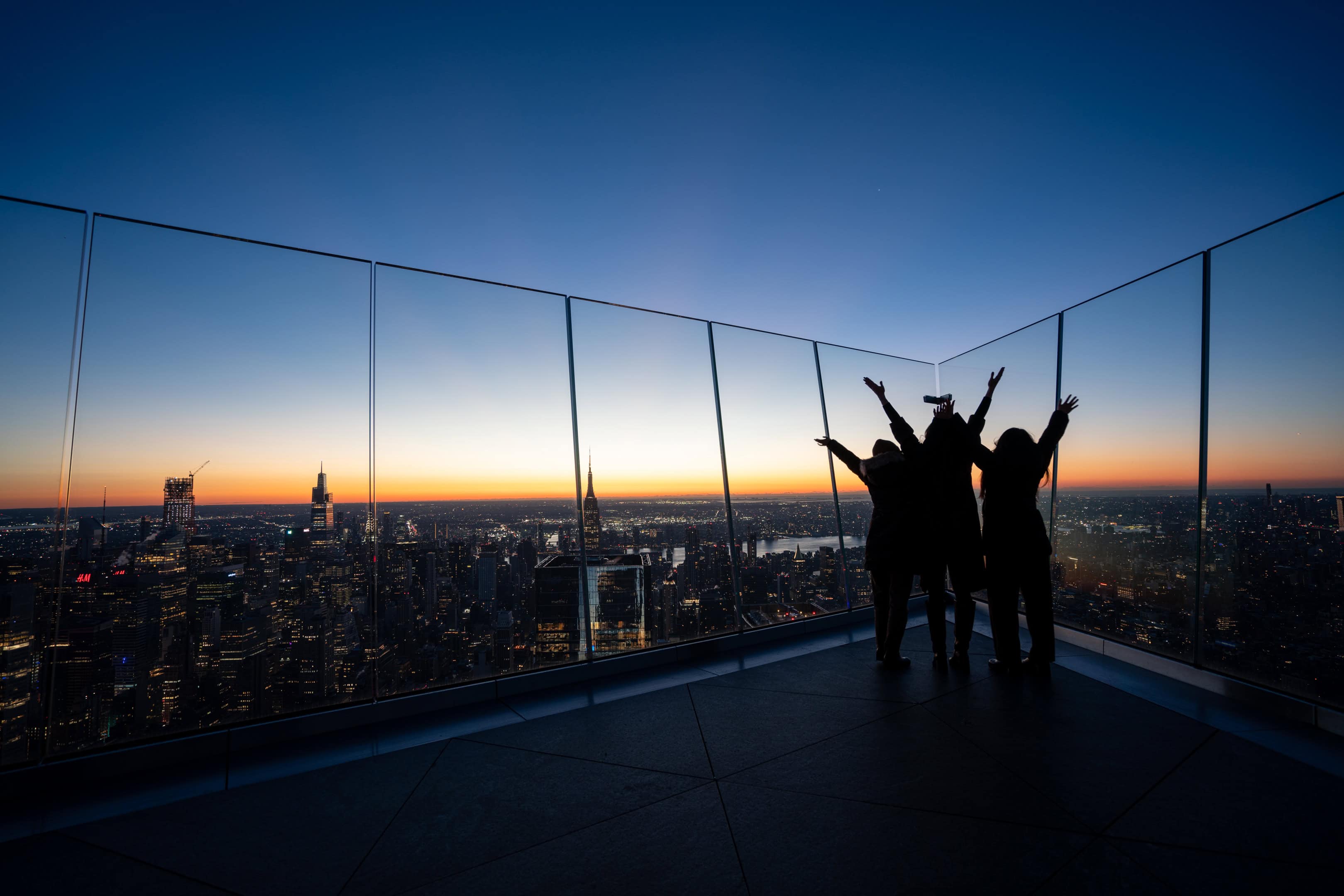 Three people raise their arms in celebration at The Edge at sunset