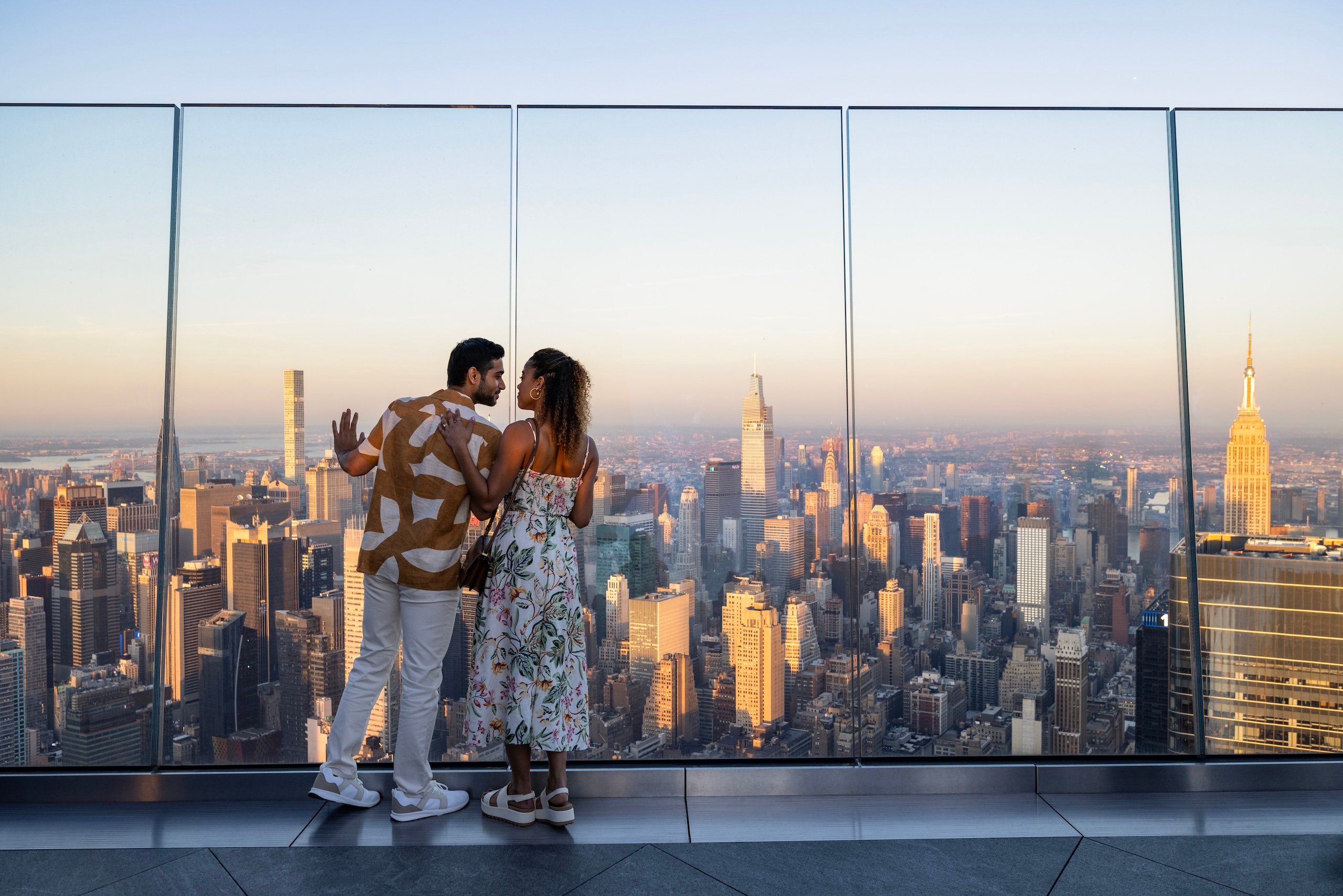 A couple embrace while looking out over New York City at sunset from The Edge