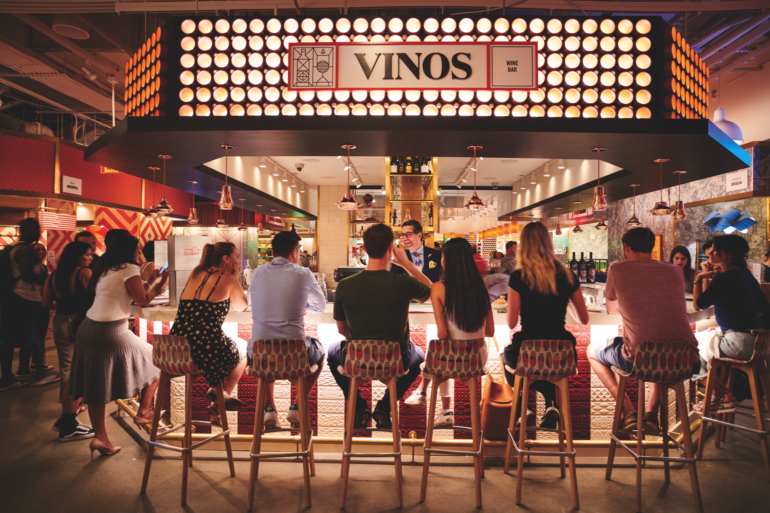 A group of people laugh and drink at the bar at Mercado Vinos