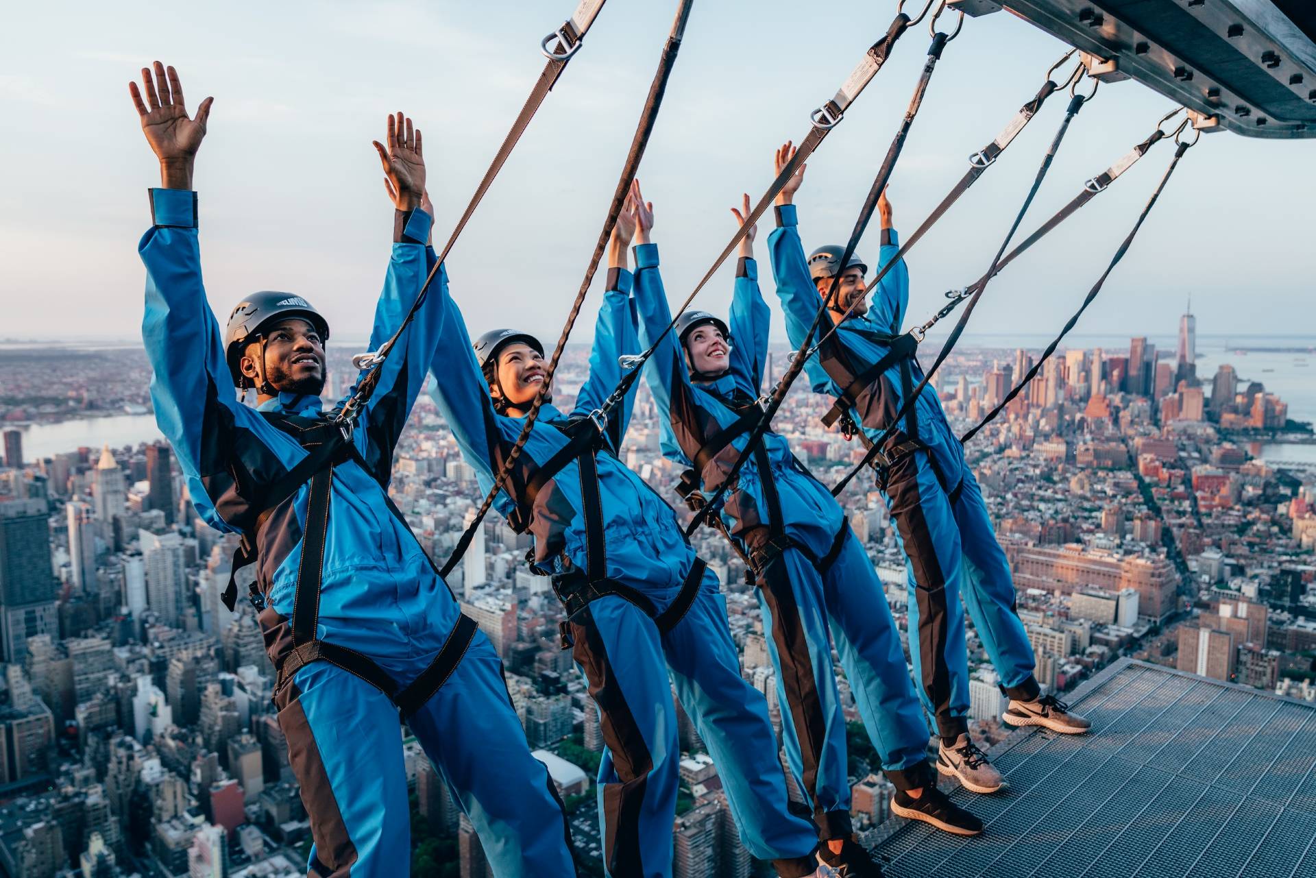 Four people raise their hands in the air in excitement as they lean back during City Climb at The Edge