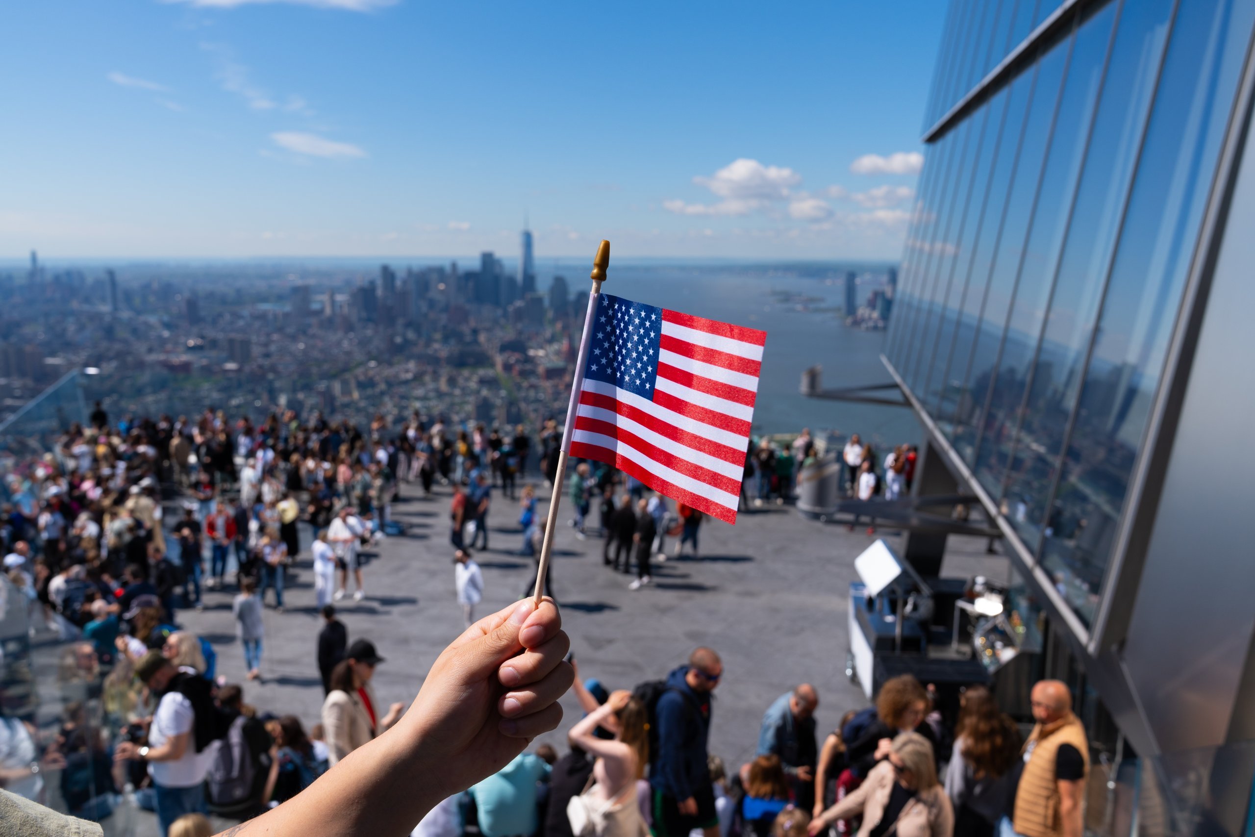 a hand holding the American flag with NYC skyline in the background from The Edge NYC