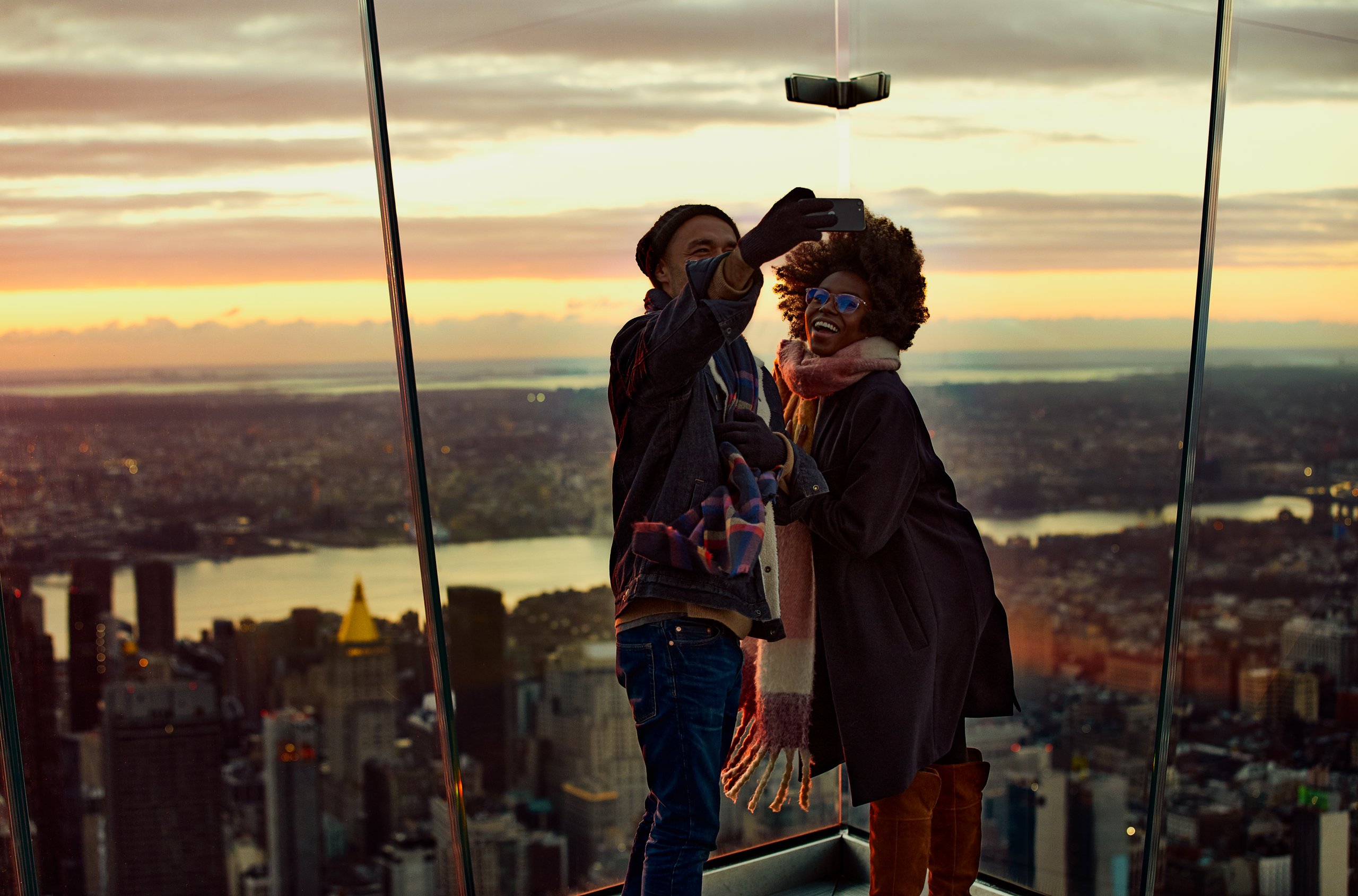 A couple posing for a selfie at the eastern point of The Edge NYC during sunset