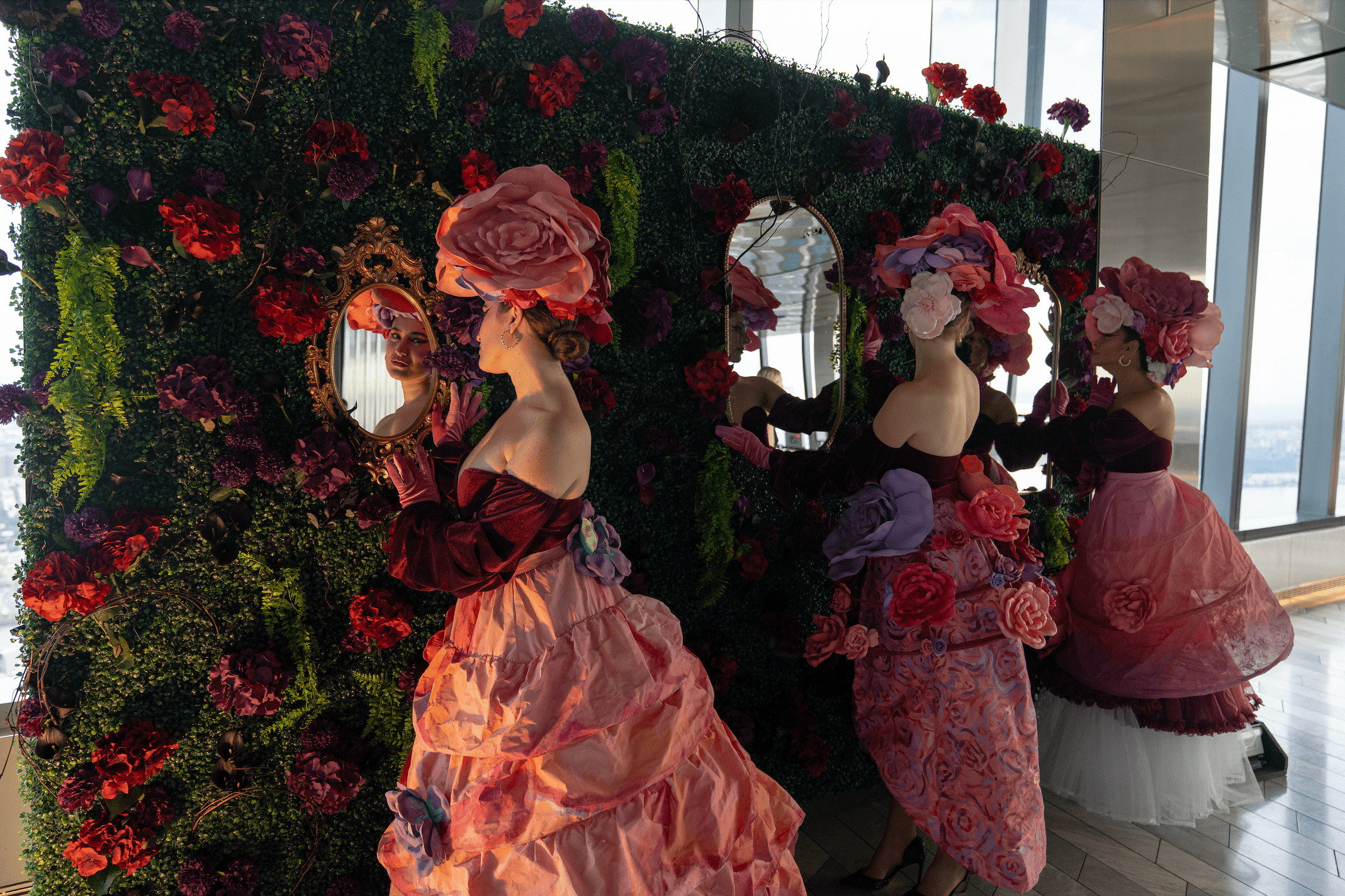 three women dressed in floral attire looking in mirrors for the garden of shadows