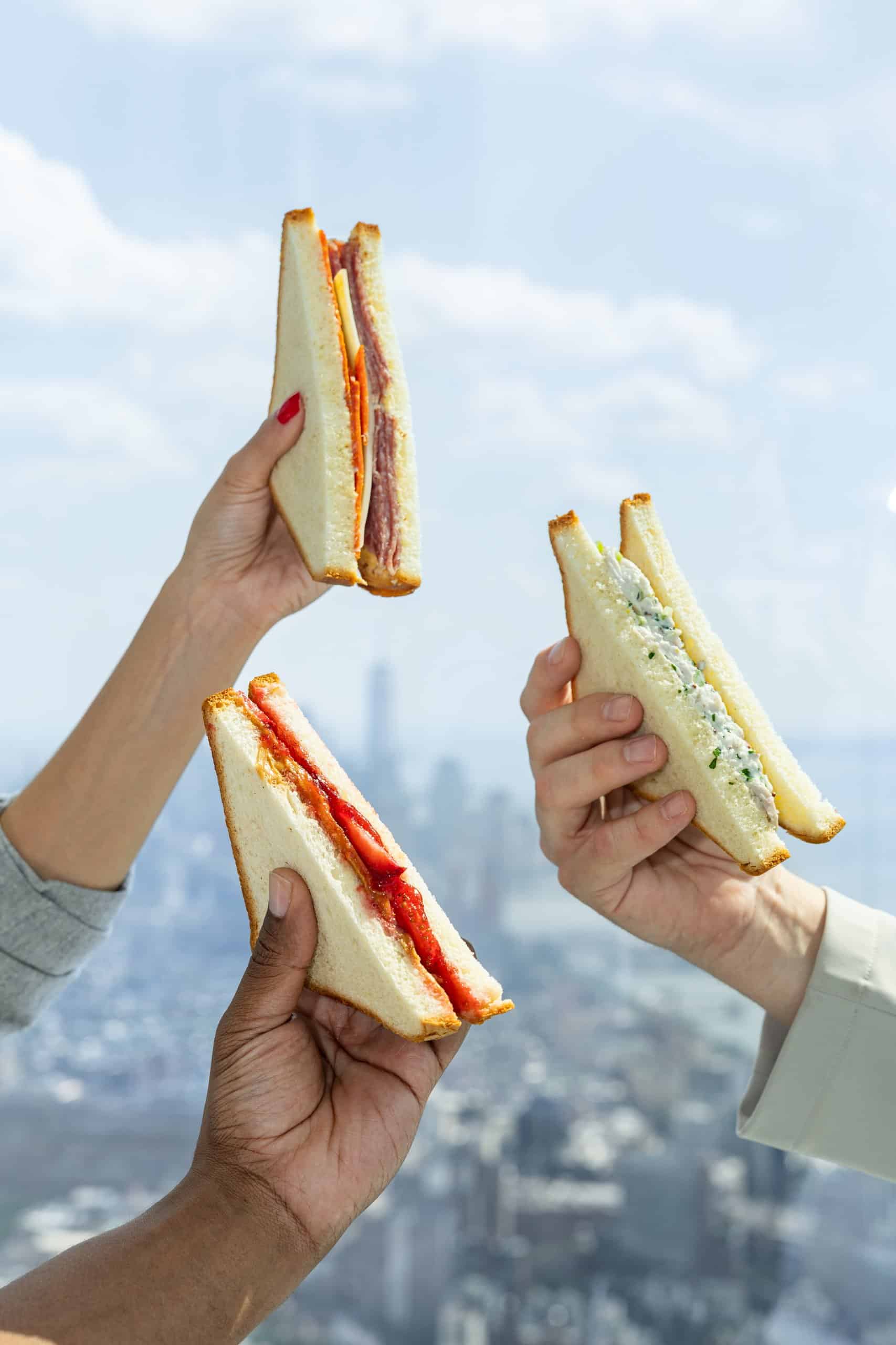 three hands holding up sandwiches from the edge nyc menu