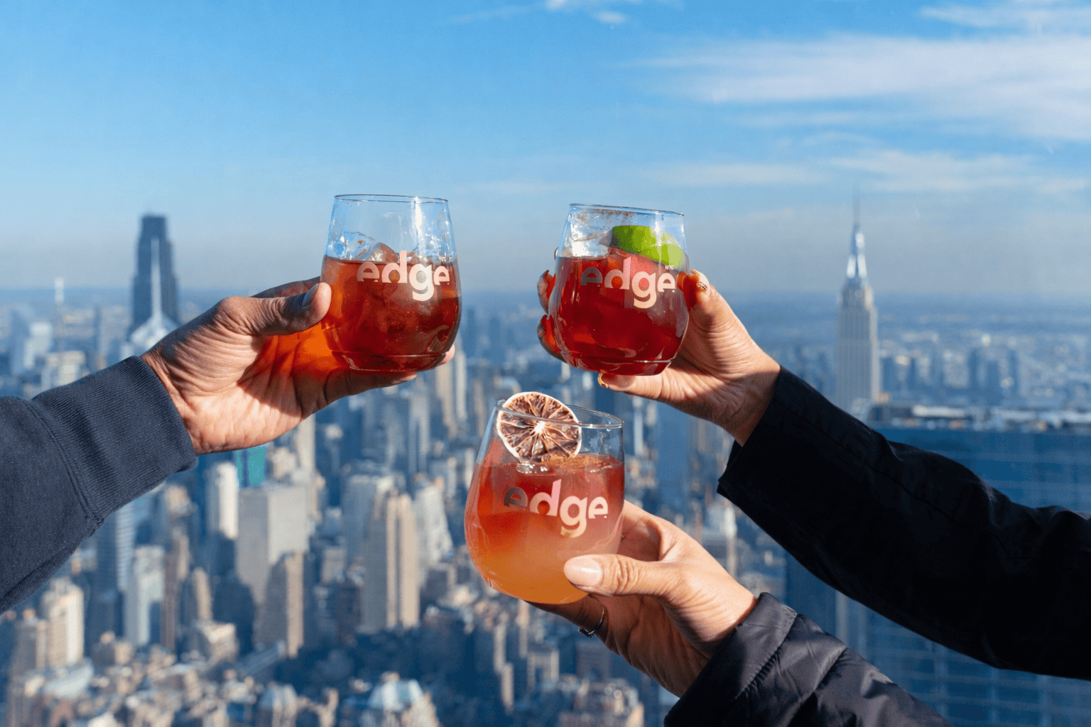 three hands holding cocktails from the edge nyc menu