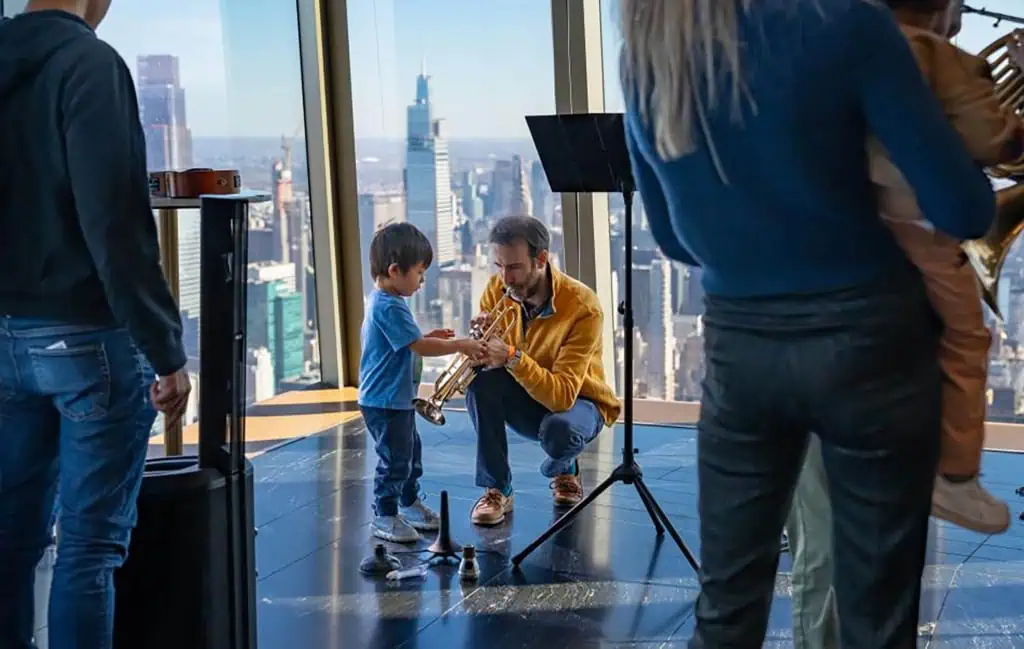 Family enjoying music at Edge NYC - Edge NYC - Edge NYC A man plays a trumpet with a child at The Edge
