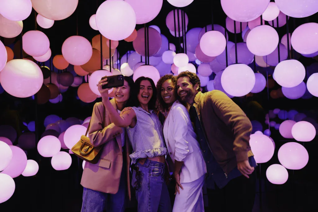 Group of friends enjoying colorful light display - Edge NYC - Edge NYC Friends taking a selfie with vibrant pink and purple lights in the background.