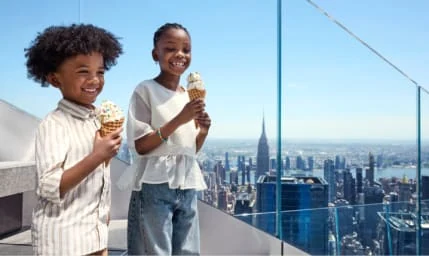 Two children enjoying ice cream with NYC skyline view from Edge NYC sky deck.